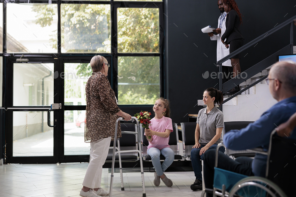Granddaughter giving bouquet of flowers to grandmother after finishing medical consultation - Stock Photo - Images