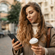 Young woman wearing autumn coat walking with smartphone and coffee cup in a city street - PhotoDune Item for Sale