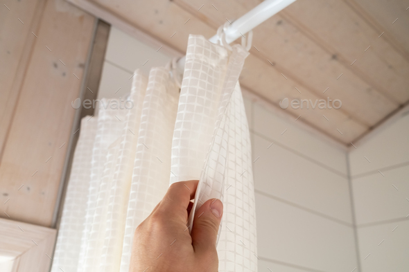 Hand closes a waterproof curtain in the bathroom, which covers the shower and prevents moisture
