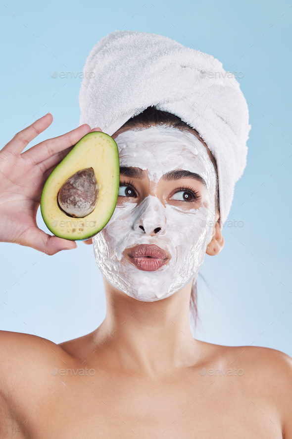Beautiful young mixed race woman wearing a face mask peel and towel while posing with an avocado. A