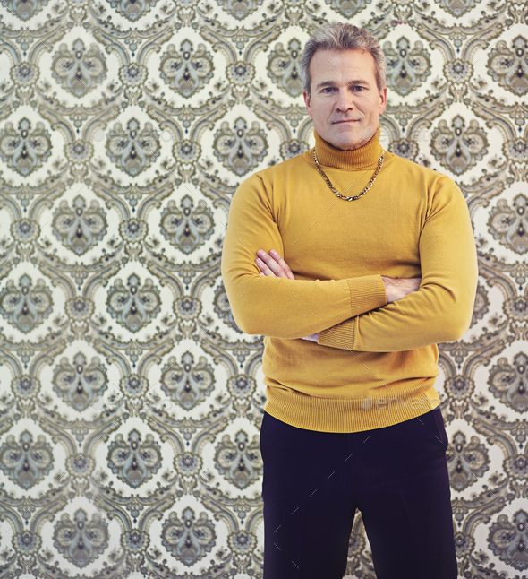 Portrait of a mature man wearing a polo neck sweater standing against a retro wallpaper background