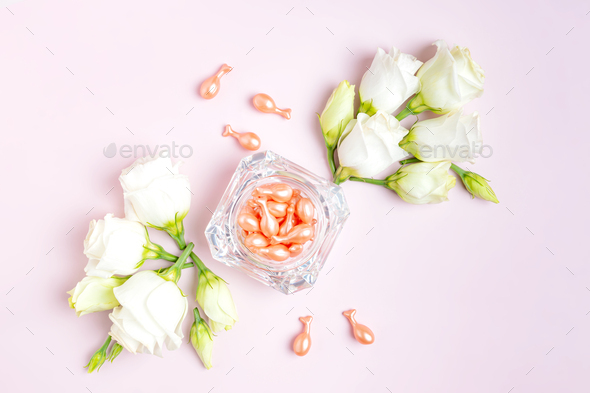 Rose Gold capsules with cosmetic oil for face in glass jar with eustoma flowers composition on pink