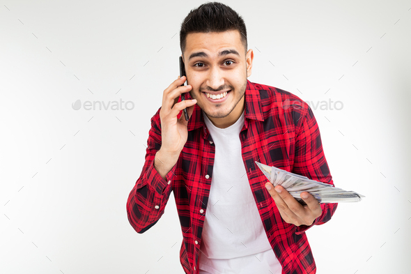 portrait of a cute guy with a bunch of money talking on the phone on a white studio background with