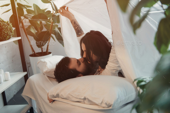 Young loving couple lying in bed cuddling looks each other under