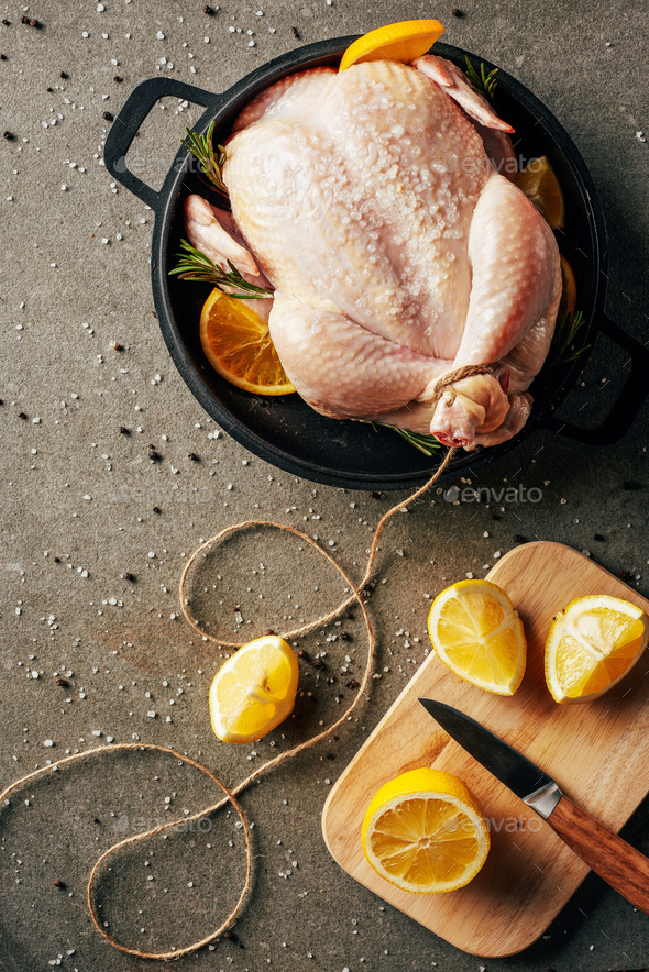 raw chicken with oranges and spices in griddle pan and cutting board with lemons and knife