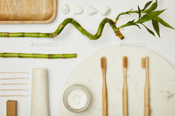 top view of ear sticks, toothpaste in tube, cosmetic cream, toothbrushes and bamboo stems on white