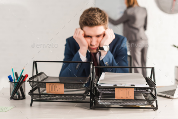 selective focus of document trays with lettering near tired man and female coworker on background,