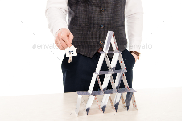 cropped view of realtor holding house keys and showing pyramid from playing cards, isolated on white