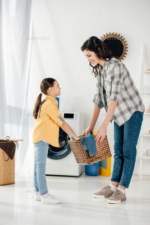 daughter in yellow shirt and mother in grey shirt holding basket and smiling in laundry room