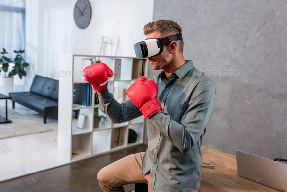 businessman wearing virtual reality headset and boxing gloves in office - Stock Photo - Images