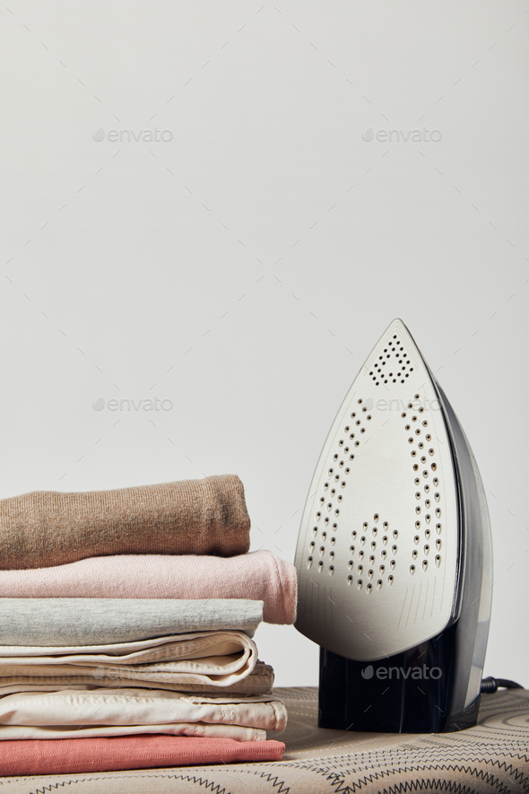 Iron and folded ironed clothes on ironing board isolated on grey Stock ...