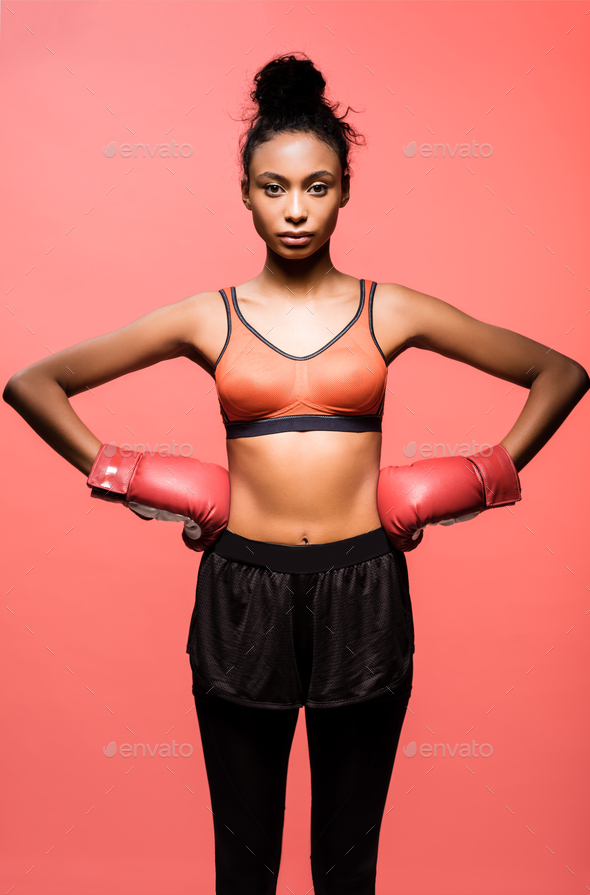 beautiful african american sportswoman in boxing gloves posing with hands akimbo and looking at