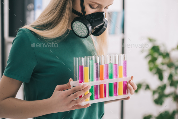 blonde woman in respiratory mask looking at colorful test tubes