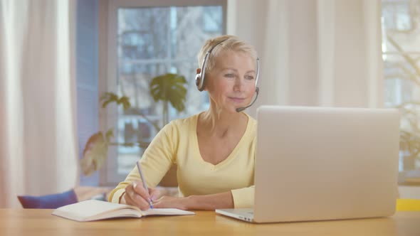 Mature Woman with Headset and Laptop Computer Having Video Conference at Home Office alt