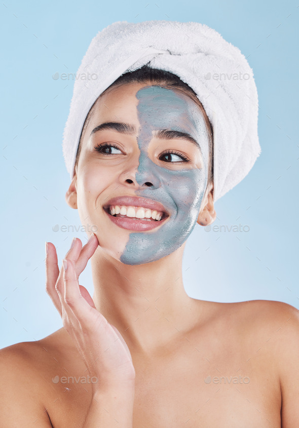 Beautiful young mixed race woman applying a face mask peel isolated in studio against a blue backgr