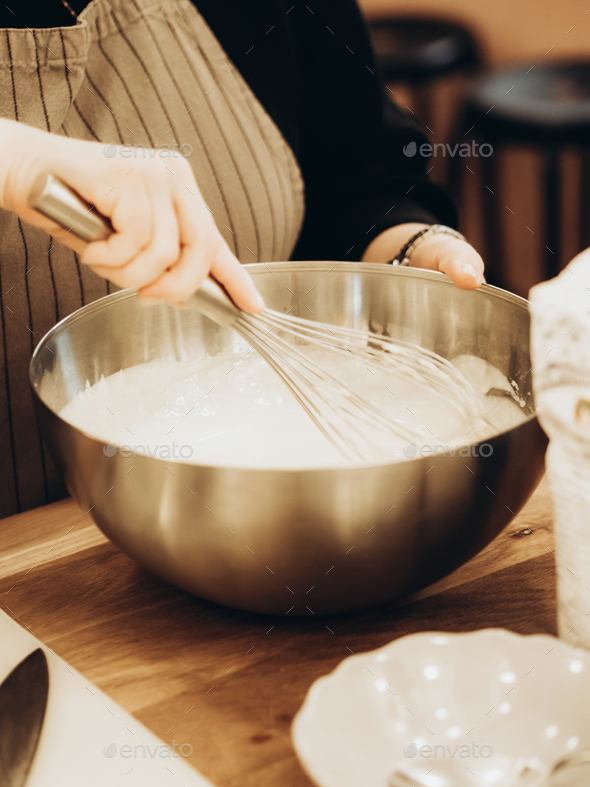 Indeterminate woman mixed batter with whisk in large metal bowl.