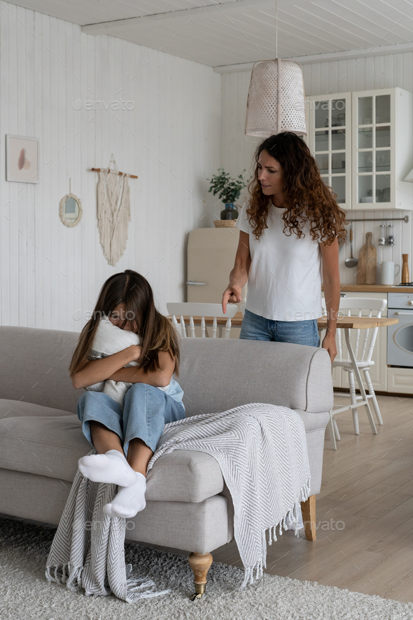 Frightened crying teenage girl sits on sofa hugging pillow and is