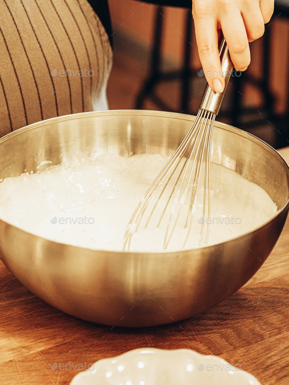 Indeterminate woman mixed batter with whisk in large metal bowl.