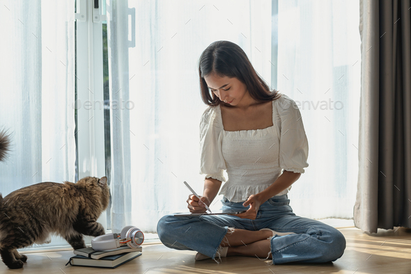 Portrait of young Asian woman sitting holding a tablet and pen with your favorite cat at home.
