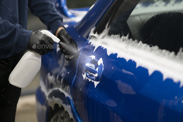 a male detailer doing work on the car, cleaning machine and applying spray on the surface