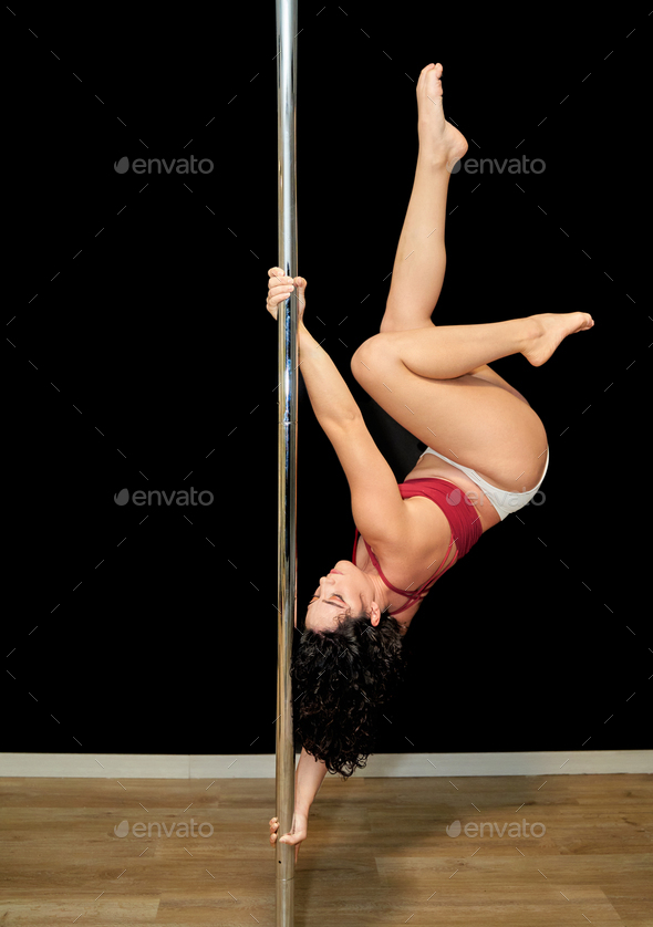 Young woman performing acrobatics on a pole dance in a rehearsal room.