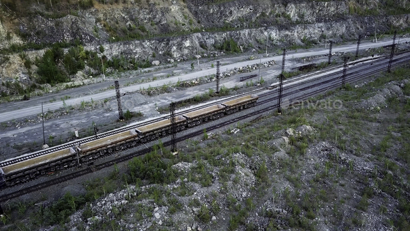 Diesel locomotive is pushing dump-car filled with rubble stone in the background of a quarry for