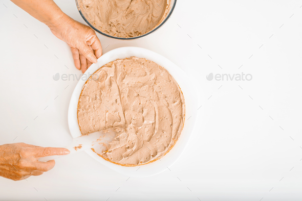 Culinary confectionery hobby. Top view female cook's wrinkled hands decorating cake with cream