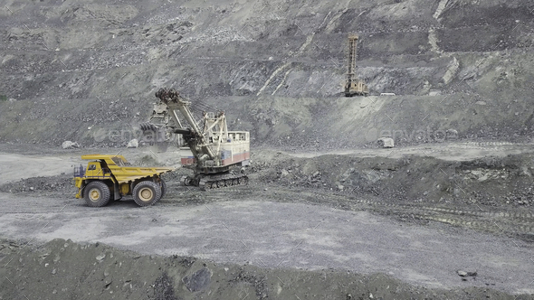 Excavator and dump truck while loading stone ore in a grey quarry, mining industry. Stock. Heavy