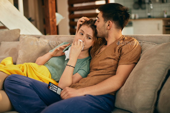 Sad woman crying while watching TV with her boyfriend at home.