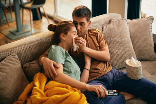 Caring man wipes girlfriend's tears while watching sad movie on TV at home.