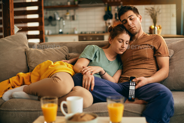 Young couple napping on the sofa while watching TV at home.