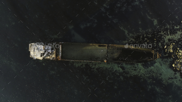 Aerial top view for wrecked ship along the rocky coast in blue water. Shot. Old sunk boat near sea