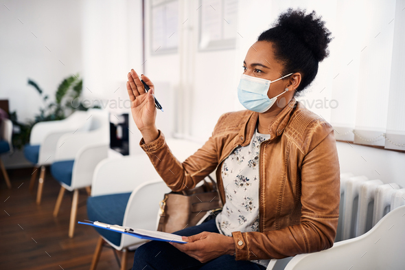 Black woman wearing protective face mask while filling paperwork before dental exam at dentist\'s.