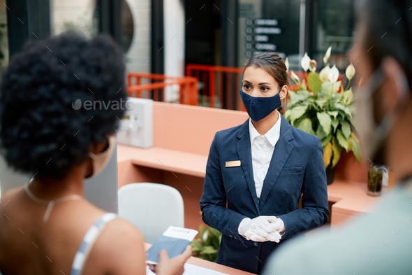 Female receptionist wearing protective face mask during guests check-in a hotel.
