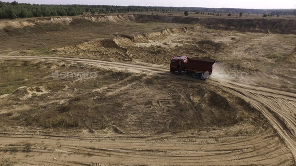 Aerial for the red big truck driving in ground quarry with flying dust behind it, industry concept