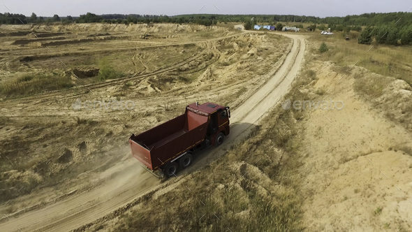 Aerial for the red big truck driving in ground quarry with flying dust behind it, industry concept