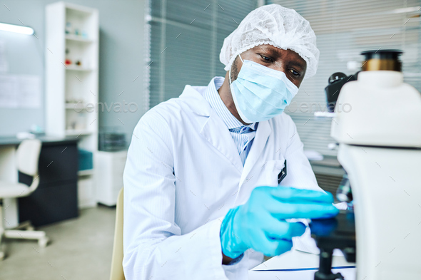 Focused black man wearing face mask doing research in laboratory