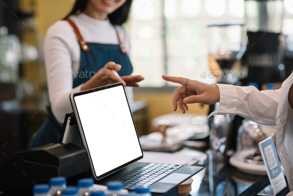Close-up of a woman ordering coffee on a tablet with a blank white screen at a coffee shop.