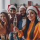 Beautiful people in Christmas hats holding champagne flutes while making selfie at home - PhotoDune Item for Sale