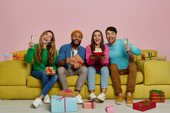Young people celebrating birthday while sitting on the couch against pink background - Stock Photo - Images
