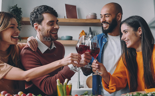 Cheerful young people toasting with wine while having dinner at home together - Stock Photo - Images