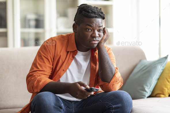 Boring african american guy sitting at home, switching tv