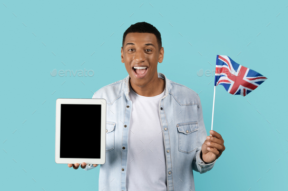 Cheerful young african american man student with open mouth show England flag, tablet with empty