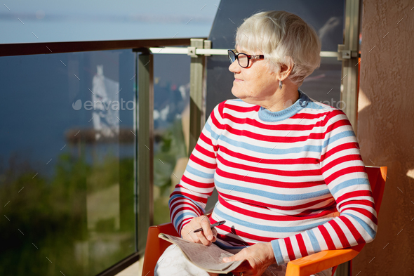 Elderly woman in glasses sitting on balcony near the sea