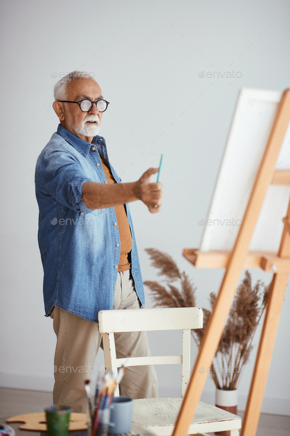 Senior artist using the rule of thumb while painting at home.