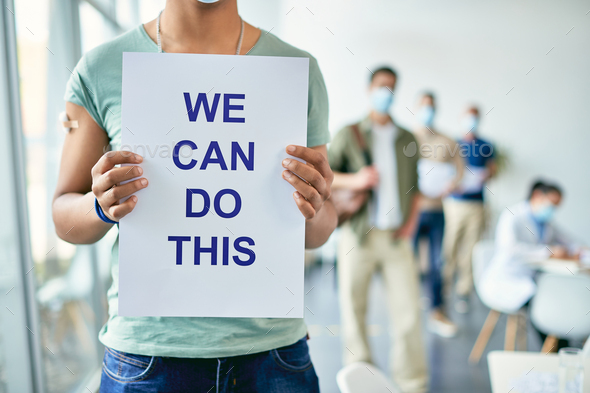  Black man holding placard with supportive \'we can do this\' message at COVID-19 vaccination center.