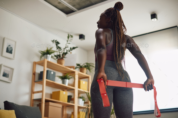 Rear view of African American athletic woman exercising with resistance band at home.