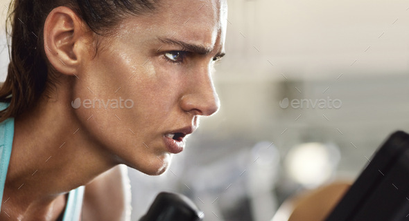 Cropped shot of a determined looking young woman working out on an elliptical machine in the gym