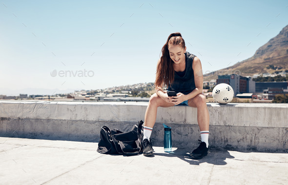 Sports woman, phone and football or soccer workout on rooftop of city building take break or rest u