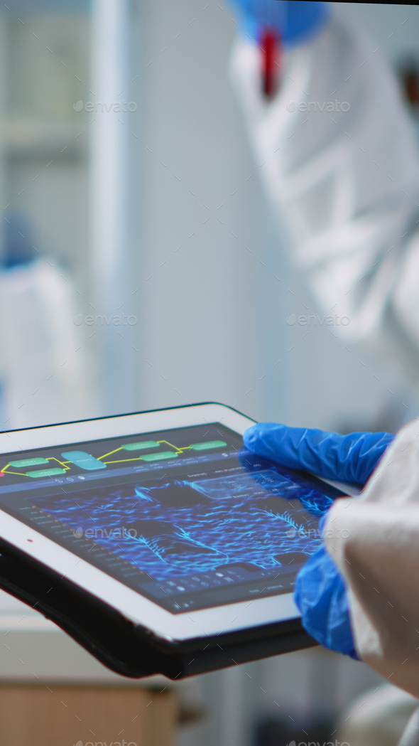 Scientist in coverall analyzing virus evolution looking on digital tablet
